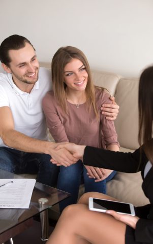 Happy cheerful couple shaking hands with female travel manager or bank worker after signing contract, personal insurance agreement, deal with advisor, lawyer or consultant, vertical